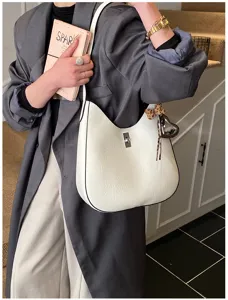 Detail shot of white leather shoulder bag with metal twist lock and cute charm, elegant style.