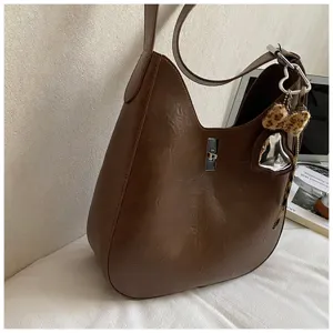 Detail shot of brown leather hobo shoulder bag featuring silver turn lock and leopard print charm.
