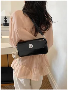 Detailed shot of a sleek black patent leather shoulder bag with chic metal lock and cute charm.