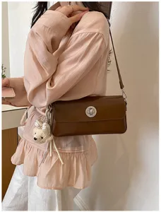 Brown leather baguette shoulder bag detail showing stylish turn lock and cute plush charm.