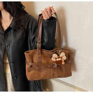 Close-up detail of the brown retro suede shoulder bag with chic buckled strap and cute plush charm.