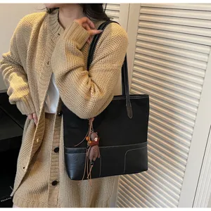 Detailed shot of a stylish black patchwork tote bag with frosted texture and a cute bear charm.