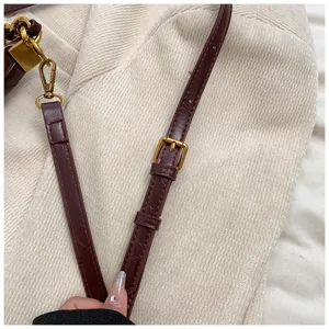 Adjustable burgundy leather handbag strap with gold tone metal buckle hardware detail.