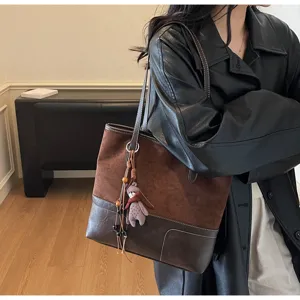 Brown suede patchwork tote bag with stylish shoulder strap and cute plush charm pendant.