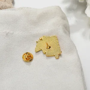Gold metal cartoon brooch pin back view with secure butterfly clutch on white canvas bag.