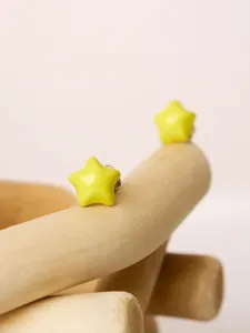Close-up detail of charming yellow star enamel stud earrings showcased on a curved wooden prop.