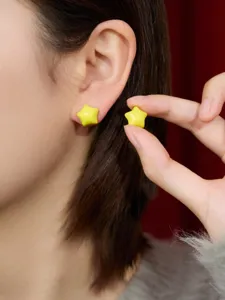 Close-up detail shot of yellow star stud earrings worn on earlobe with hand holding matching piece.