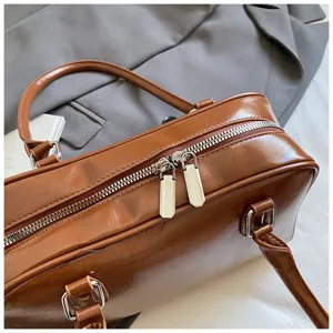 Dettaglio in primo piano di borsa bowling in ecopelle marrone con doppie cerniere lampo metalliche.