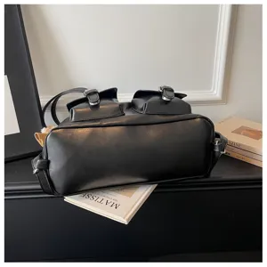 Detail view of black faux leather women bag with dual front pockets and metal buckle closure.