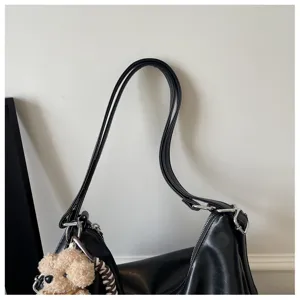 Detailed shot of a stylish black shoulder bag with a cute fuzzy bear pendant and metal hardware.