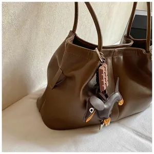 Close-up detail of brown leather tote bag with cute chocolate and dog charms, stylish bag.