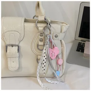 Close-up detail of white vintage faux leather shoulder handbag with cute charms and ribbons.