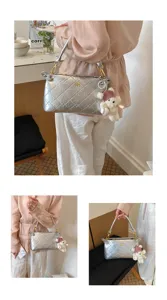 Close-up detail of silver quilted shoulder bag featuring cute bear pendant and sleek metal handle.