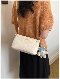 Detail view of a stylish white quilted underarm shoulder bag with a cute bear pendant.