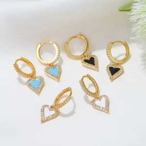 Gros plan détaillé de boucles d'oreilles créoles dorées en zircone avec pendentifs cœur émaillés.