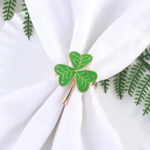 Close-up detail of a green enamel shamrock napkin ring decorated with rhinestones on white cloth.