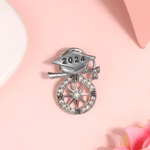 Nahaufnahme Detail einer silbernen Abschluss Broche mit 2024 Kappe und Strass Kompass.