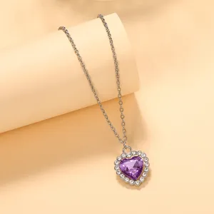 Colgante de cadena plateada con cristal morado en forma de corazón y pedrería brillante.
