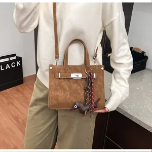 Brown leather shoulder bag detail featuring top handles, metal clasp and cute dog charm.