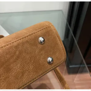 Detailed bottom view of brown leather women shoulder bag with metal feet and fine stitching.