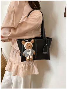 Detail view of a stylish black tote shoulder bag with contrast stitching and cute bear charm.