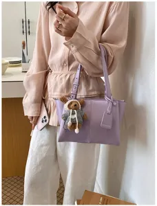 Close-up detail of the elegant light purple shoulder tote bag featuring a cute knitted bear charm.