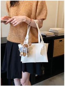 White leather underarm shoulder tote bag detail view with cute plush bear pendant accessory.