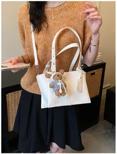 Close-up view of white leather tote shoulder bag showcasing cute plush bear charm and details.