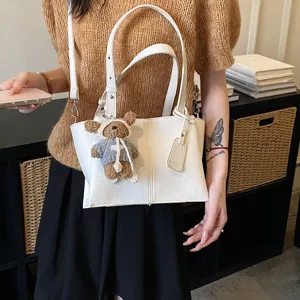 Stylish white leather underarm shoulder bag with cute teddy bear pendant for women commuting.
