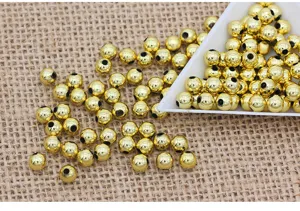 Detail shot of shiny gold ABS plastic loose beads scattered on burlap with a white tray.