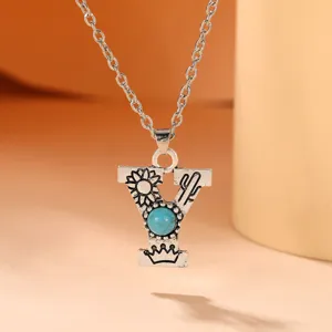 Detail view of a boho style silver letter Y pendant necklace with turquoise and cactus.