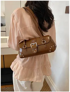 Bolso de hombro bajo el brazo de charol marrón con hebilla de metal y detalles de tachuelas.