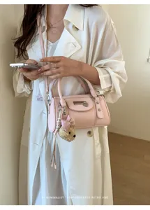Detailed view of trendy pink cylindrical handbag featuring chic bow bear charm and hardware.