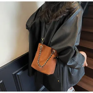 Vue détail sac seau en daim marron, bandoulière chaîne élégante et texture douce.