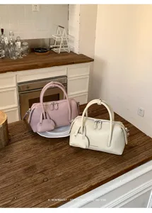 Detailed view of chic pebbled leather Boston handbag in pink and beige, stylish shoulder bag.