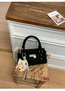 Detailed shot of black retro bowling handbag with metal heart lock and cute plush dog pendant.