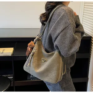 Detailed view of the stylish grey shoulder bag with a metal triangle logo and cute bear charm.