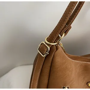 Close-up detail of stylish brown leather shoulder bag strap with gold metal hardware and stitching.