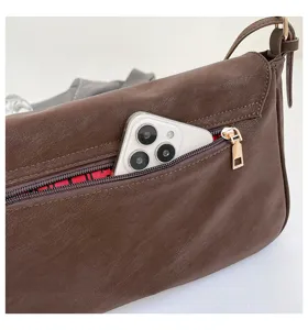 Brown vintage leather shoulder bag detail, showing zipper pocket, phone and inner plaid lining.