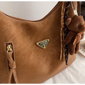 Brown PU leather shoulder tote bag with front zip pocket, cute bear pendant and stylish tassel.