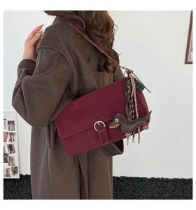 Retro suede shoulder bag featuring a cute dachshund charm and metal buckle design. Detail view.