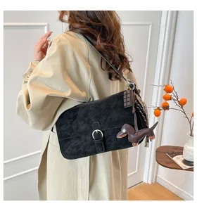 Detail view of black suede retro underarm shoulder bag with cute dachshund charm and metal buckle.