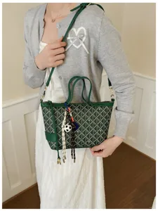 Vue détaillée du sac seau bandoulière en toile verte avec des charms tissés élégants.