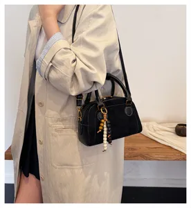Black leather bowling bag with bead pendant, stylish shoulder bag for daily casual wear.