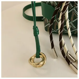 Gros-plan du sac-seau vert avec toile chevron, cordon en cuir et anneaux en metal dores.