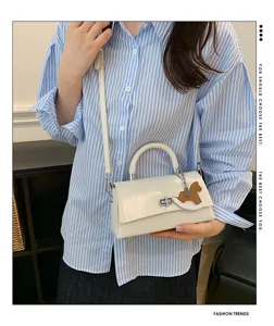 Gedetailleerd overzicht van een elegante witte handtas met paardenhangel en draaisluiting.
