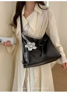 Vista dettagliata di una elegante borsa a tracolla nera con ciondolo floreale argento.