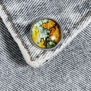 Gedetailleerde close-up van vintage wereldkaart glas cabochon broche badge op denim stof.