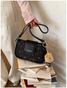 Vue détaillée d'un sac bandoulière noir à motif d'étoiles avec rabat et pendentif ours.