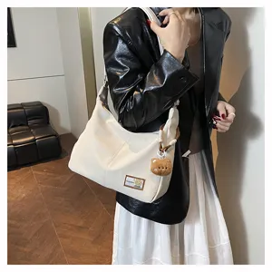 White dumpling shoulder bag detail featuring soft material and cute bear pendant charm accessory.